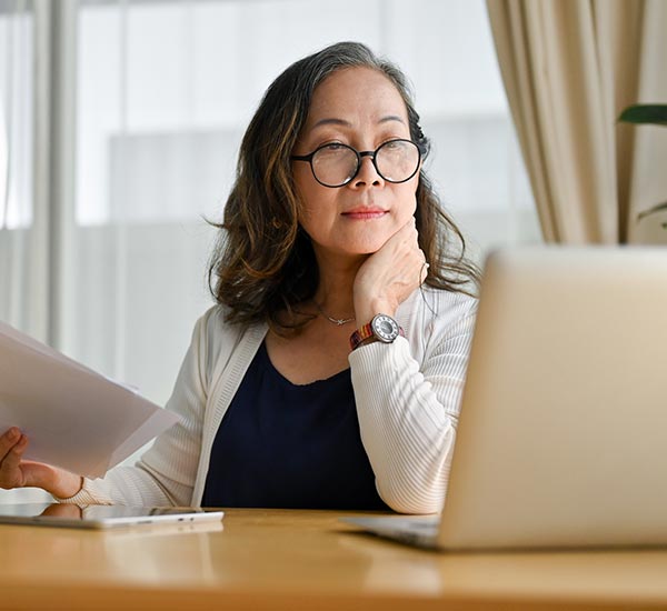 Woman using a laptop while holding papers.