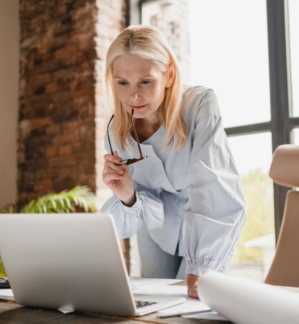 woman holding glasses looking at laptop