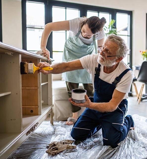 Two people putting finish on a kitchen cupboard